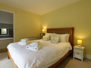 A bedroom with a wooden bed frame white bedding rolled towels bedside tables and lamps at Quill Farm Barn in Campsea Ashe
