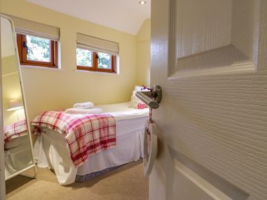 A bedroom with a single bed covered with a red and white checkered blanket and folded towels near two windows at Quill Farm Barn Campsea Ashe
