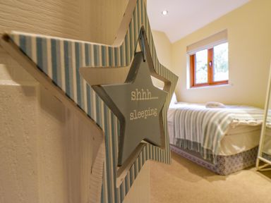 A bedroom with a single bed next to a window and a hanging star-shaped sign on a door at Quill Farm Barn in Campsea Ashe