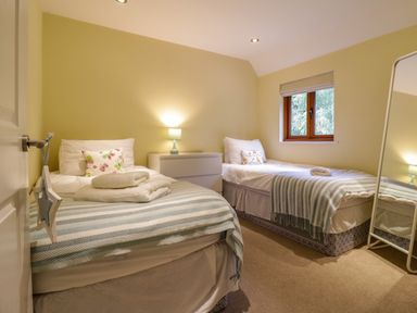 A bedroom with two single beds a window a dresser a lamp and a full length mirror at Quill Farm Barn in Campsea Ashe