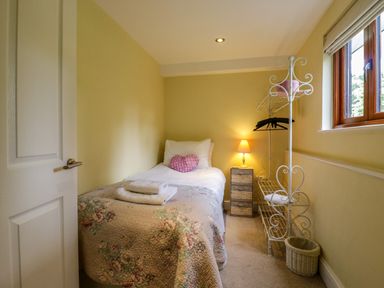 A small bedroom with a single bed a bedside table with a lamp and a metal clothes rack near a window at Quill Farm Barn in Campsea Ashe