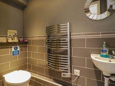 A bathroom with a toilet sink chrome towel radiator and round mirror at Quill Farm Barn in Campsea Ashe