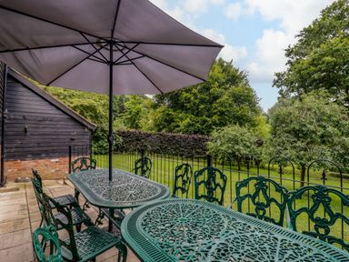 An outdoor patio with two metal tables six chairs and a large umbrella overlooking a garden at Quill Farm Barn in Campsea Ashe