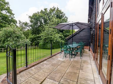 A patio with outdoor dining table and chairs under an umbrella next to a house and a grassy yard at Quill Farm Barn in Campsea Ashe
