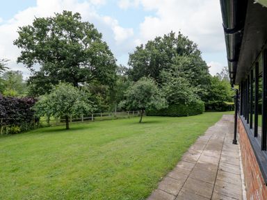 A garden with grass lawn small trees and a paved path beside a building at Quill Farm Barn in Campsea Ashe