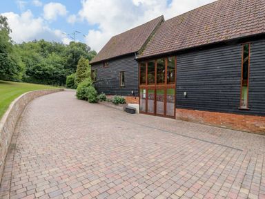 A paved driveway next to a building with dark wooden siding and large windows at Quill Farm Barn in Campsea Ashe