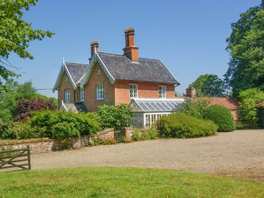 A brick house with a glass conservatory surrounded by bushes and trees at Church Farm Dunwich Near Westleton