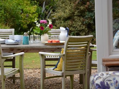 An outdoor wooden table with chairs on a gravel surface with plates glasses flowers and fruit at Church Farm Dunwich Near Westleton