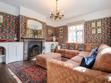 A living room with a large L shaped brown sofa and ottoman by a fireplace and a patterned rug at Church Farm Dunwich Near Westleton