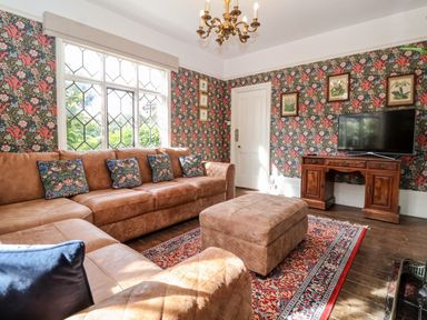 A living room with a brown leather sofa and ottoman a patterned rug a wooden TV stand with a television and floral wallpaper at Church Farm Dunwich Near Westleton