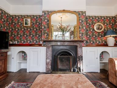 A living room with a fireplace mirror and floral wallpaper at Church Farm Dunwich Near Westleton