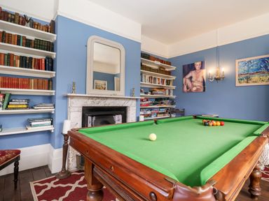 A room with a pool table in the center blue walls with bookshelves fireplaces and paintings at Church Farm Dunwich Near Westleton