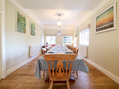 A dining room with a long table covered with a patterned tablecloth and wooden chairs at Church Farm Dunwich Near Westleton