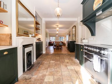 A kitchen with tiled floor green cabinets and a stove overlooking a dining area with wooden table and chairs at Church Farm Dunwich Near Westleton