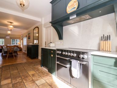 A kitchen with a stove green cabinets a knife block and dining table at Church Farm Dunwich Near Westleton