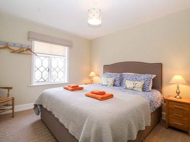 A bedroom with a double bed with pillows and orange towels bedside tables with lamps a window with hangers and a wooden chair at Church Farm Dunwich Near Westleton