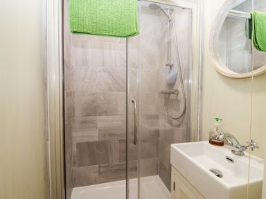 A bathroom with a shower enclosure a sink with a faucet and handwash and a round mirror at Church Farm Dunwich Near Westleton