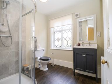 A bathroom with a shower, toilet, window, and sink cabinet at Church Farm, Dunwich Near Westleton