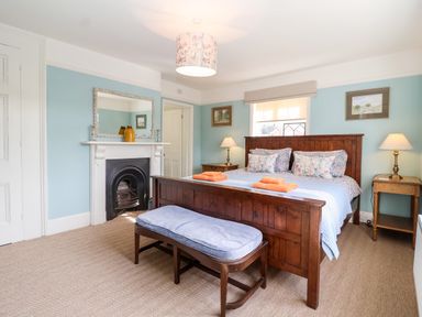 A bedroom with a wooden bed and bench a fireplace two bedside tables with lamps and paintings on the wall at Church Farm Dunwich Near Westleton