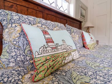 A bed with patterned bedding and two decorative pillows with lighthouse designs at Church Farm Dunwich