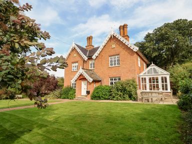 A red brick house with white trim windows and a glass conservatory surrounded by green lawn and trees at Church Farm Dunwich Near Westleton
