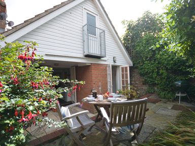 A patio area with a wooden table and chairs outside a house with a white upper wall in Mariners Cottage King Street Aldeburgh