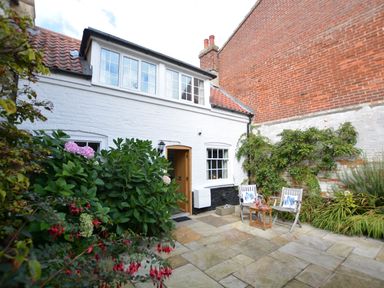 A white brick house with a tiled roof and patio with two chairs and plants at Mariners Cottage King Street Aldeburgh