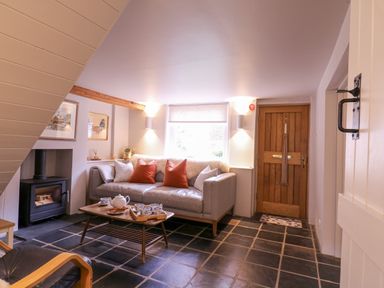 A sitting area with a sofa and cushions a coffee table with tea set a wood stove and wooden front door at Mariners Cottage King Street in Aldeburgh