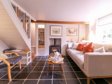 A living room with a sofa with cushions a coffee table with tea set a fireplace and a chair at Mariners Cottage King Street Aldeburgh