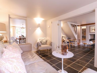 A sitting room with a leather sofa, armchairs, a small round table with glasses and a bottle, and a view into a dining area at Mariners Cottage King Street Aldeburgh