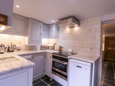 A kitchen with grey cabinets a built-in oven a dishwasher a stovetop and small appliances at Mariners Cottage King Street in Aldeburgh