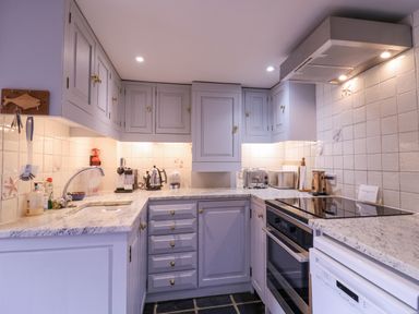 A kitchen with light gray cabinets white tiled walls a sink countertop appliances including a toaster kettle and an oven at Mariners Cottage King Street Aldeburgh