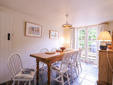 A dining room with a wooden table surrounded by six white chairs a lamp and glass doors at Mariners Cottage King Street Aldeburgh