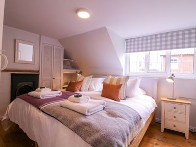 A bedroom with a double bed, bedside table with lamp, window with checkered blind at Mariners Cottage King Street in Aldeburgh