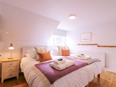 A bedroom with a double bed bedside table and lamp wooden floor and a window with checked curtains at Mariners Cottage King Street in Aldeburgh