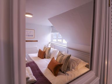 A bedroom with a bed, pillows, blanket, window, and framed picture at Mariners Cottage, King Street in Aldeburgh