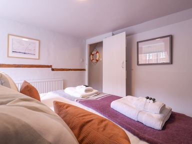A bedroom with a bed with folded towels on a purple blanket and cushions with framed pictures on the walls at Mariners Cottage King Street in Aldeburgh