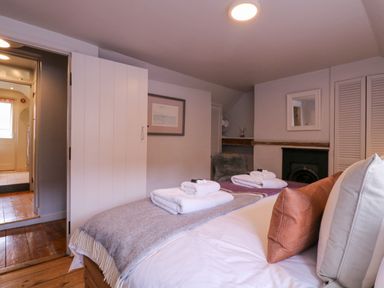 A bedroom with a bed with pillows and folded towels and a fireplace at Mariners Cottage King Street Aldeburgh