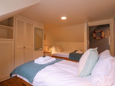 A bedroom with two beds white bedding and a lifebuoy on the wall at Mariners Cottage King Street Aldeburgh