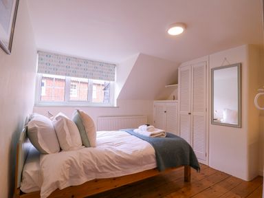 A bedroom with a bed pillows towels wardrobe and a mirror at Mariners Cottage King Street in Aldeburgh