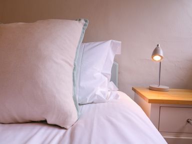 A bed with a large pillow and white bedding next to a wooden nightstand with a small lamp at Mariners Cottage King Street in Aldeburgh