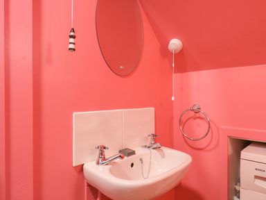 A bathroom sink with two taps a round mirror and a towel ring at Mariners Cottage King Street in Aldeburgh