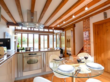 A kitchen and dining area with a glass table set for four and wooden beams on the ceiling at Two Chantry Barns Orford