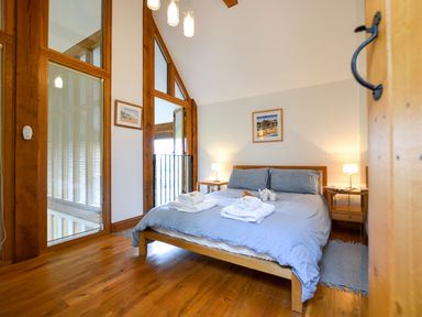 A bedroom with a wooden bed and blue bedding two bedside tables with lamps wooden floor and wall art at Two Chantry Barns Orford