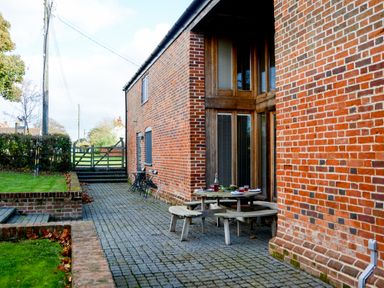 A patio area with a round wooden picnic table and chairs outside a brick building at Two Chantry Barns Orford