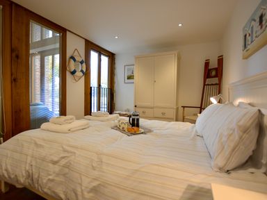 A bedroom with a bed set with white linens towels and breakfast tray by windows and a white wardrobe at Two Chantry Barns Orford