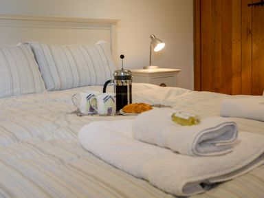 A bed with striped bedding towels and a breakfast tray with coffee and croissants at Two Chantry Barns Orford