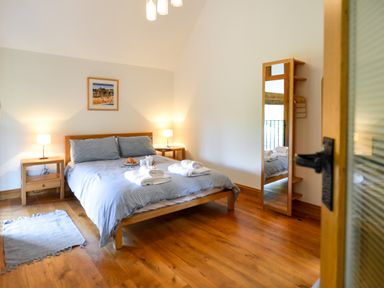 A bedroom with a bed and bedside tables with lamps and a standing mirror at Two Chantry Barns Orford