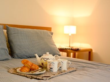 A bed with checkered pillows and a tray holding a teapot croissants and cups at Two Chantry Barns Orford