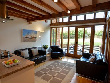 A living room with leather sofas and armchair a floor lamp and a painting above a sofa at Two Chantry Barns Orford